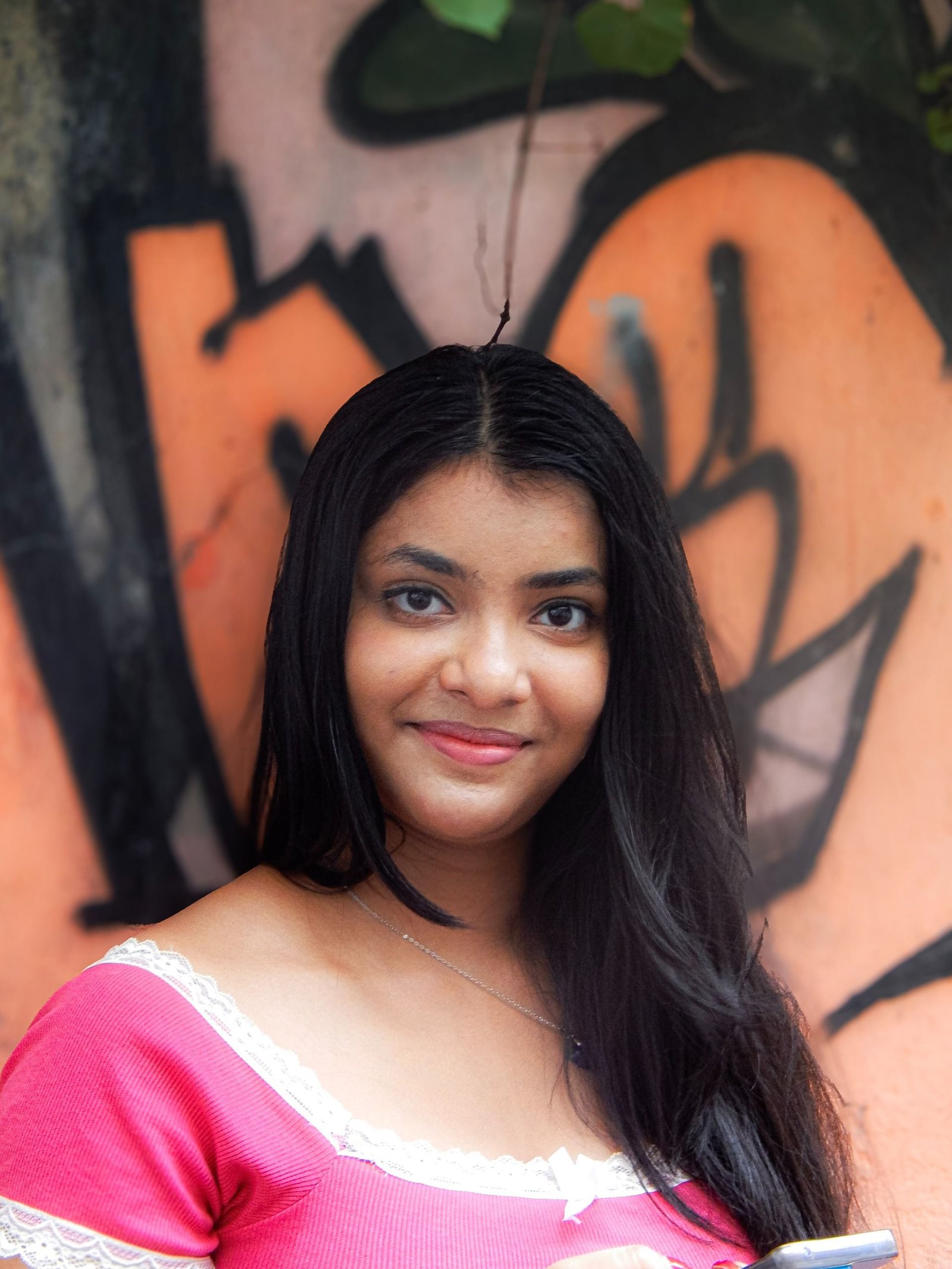 A young woman poses outdoors against colorful graffiti in India, exuding confidence and warmth.